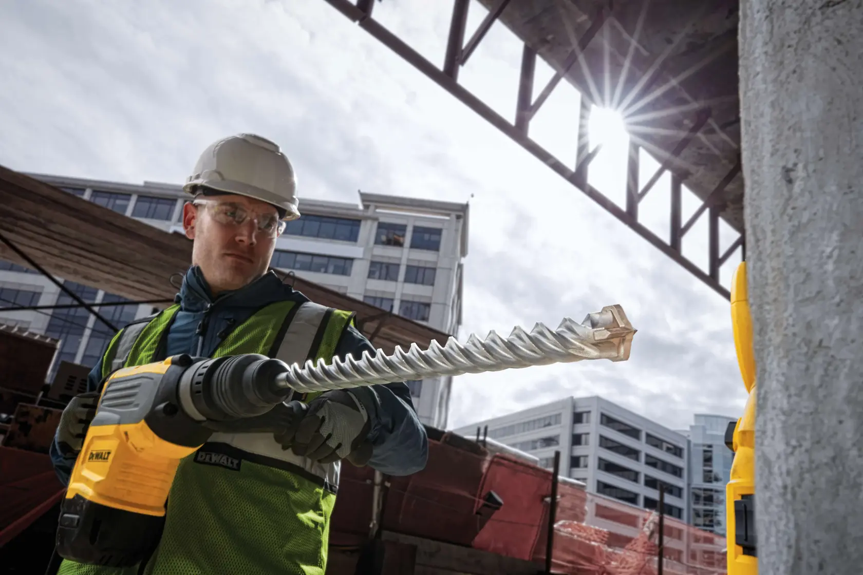 DEWALT DT60835 drill bit in use at a construction site. Worker wearing safety gear outdoors near buildings.