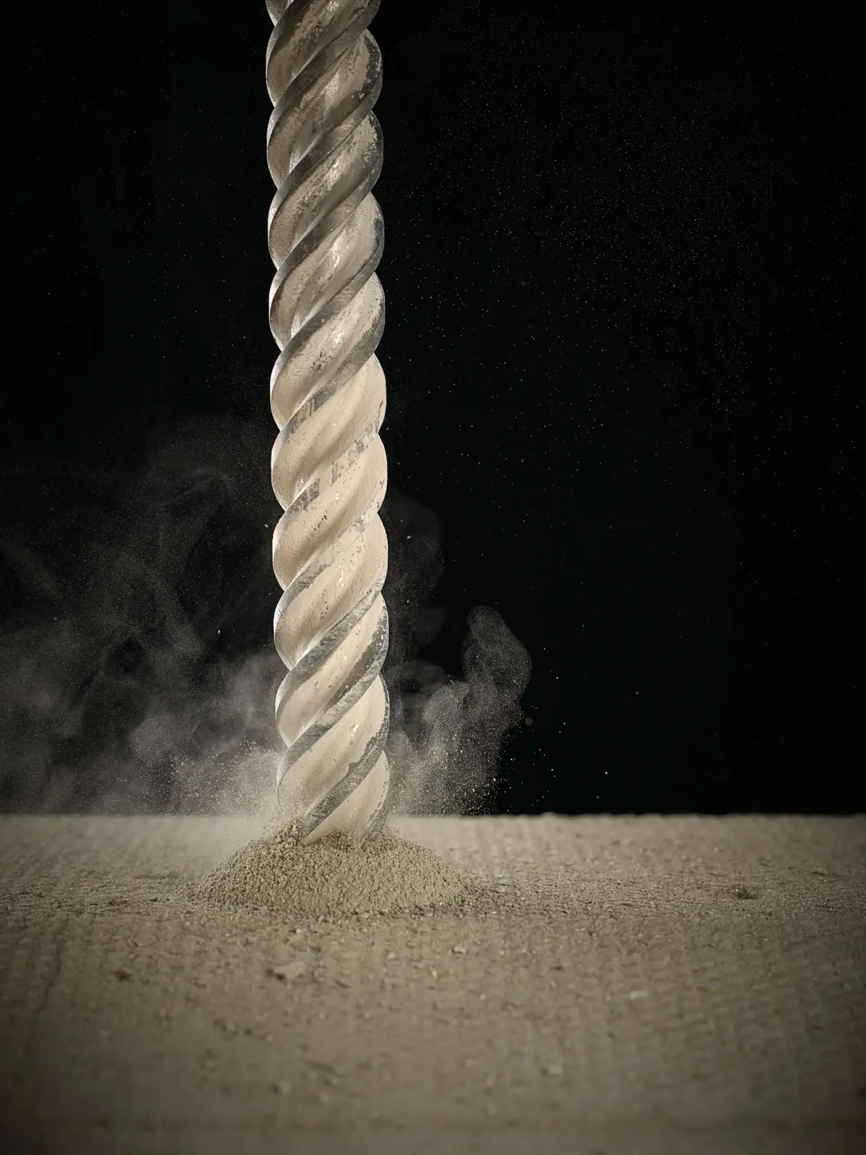 Close-up of a DEWALT drill bit boring into concrete, creating dust and debris against a dark background.