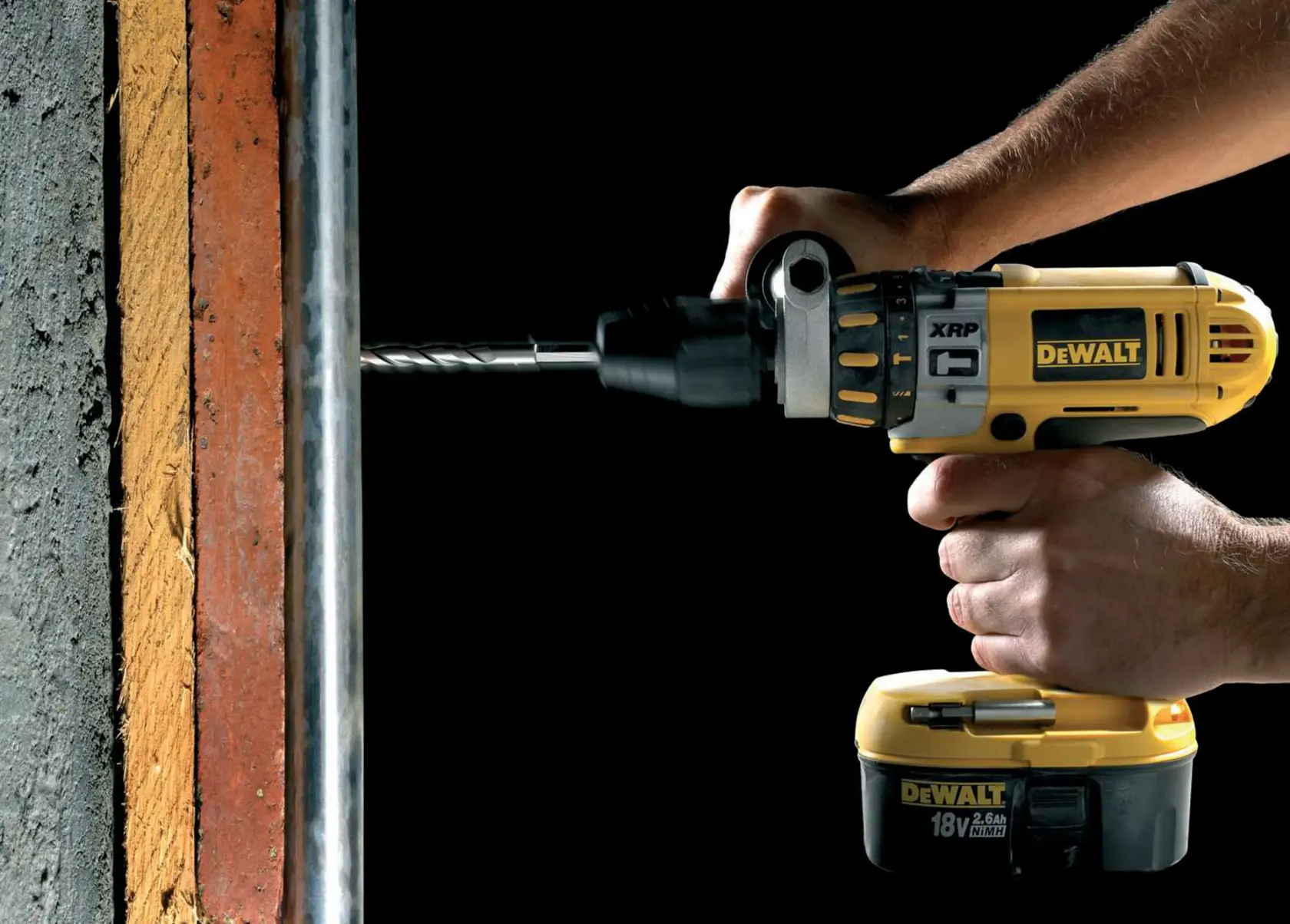A DEWALT cordless drill in use, drilling into a concrete wall with a person's hands holding it.