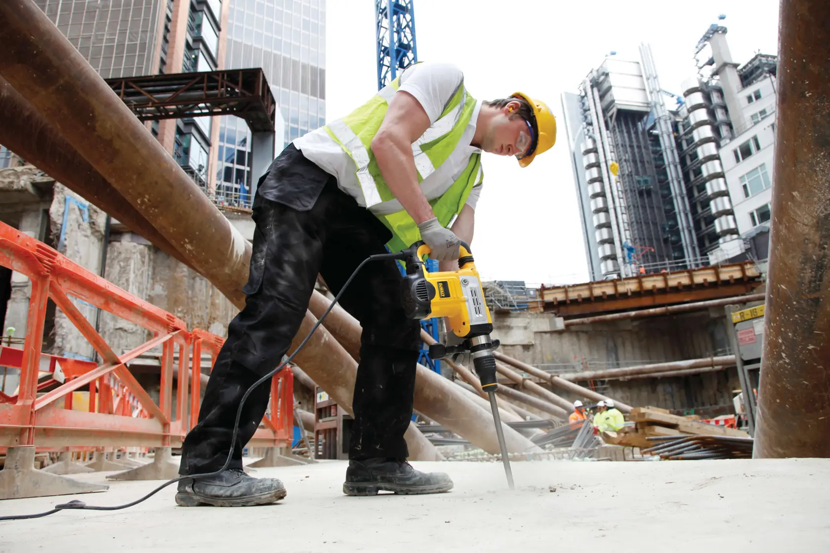 Worker using a DEWALT DT6825 tool to drill concrete at a construction site with buildings in the background.