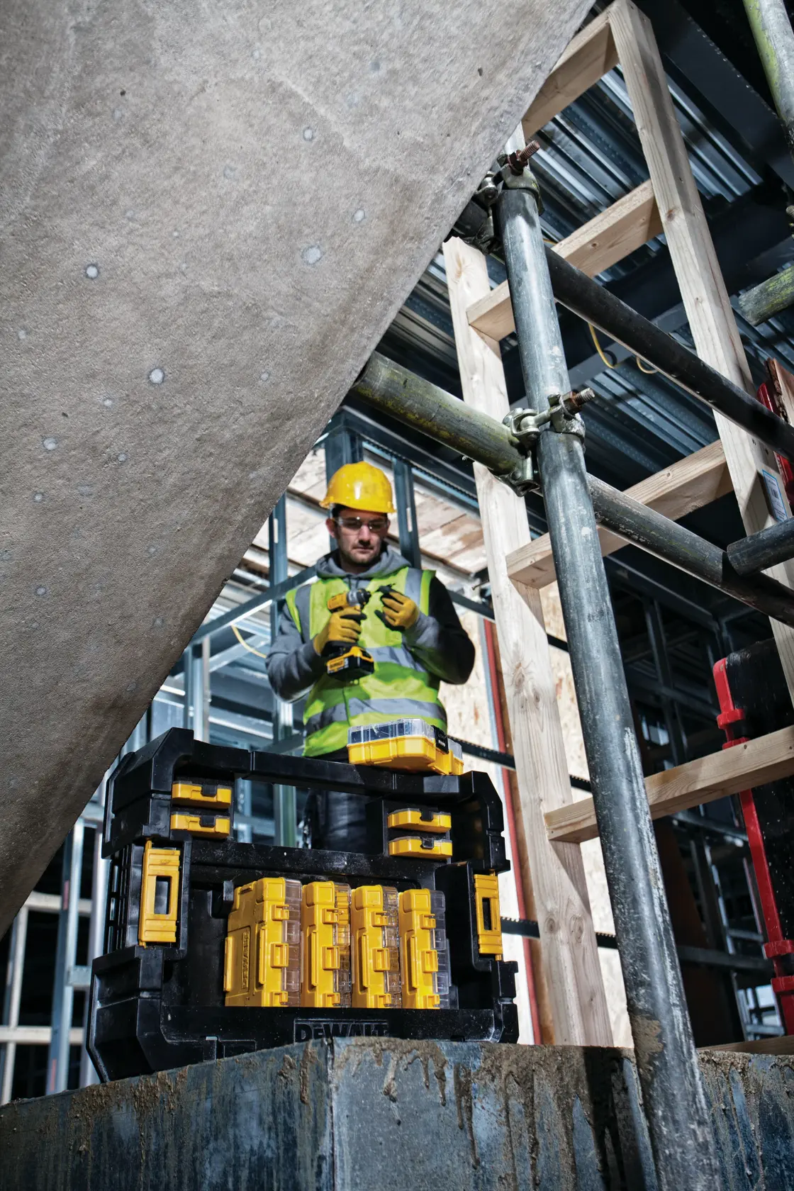 DEWALT DT70716 tool kit on site with worker in safety gear, scaffolding and wooden structure visible in background.