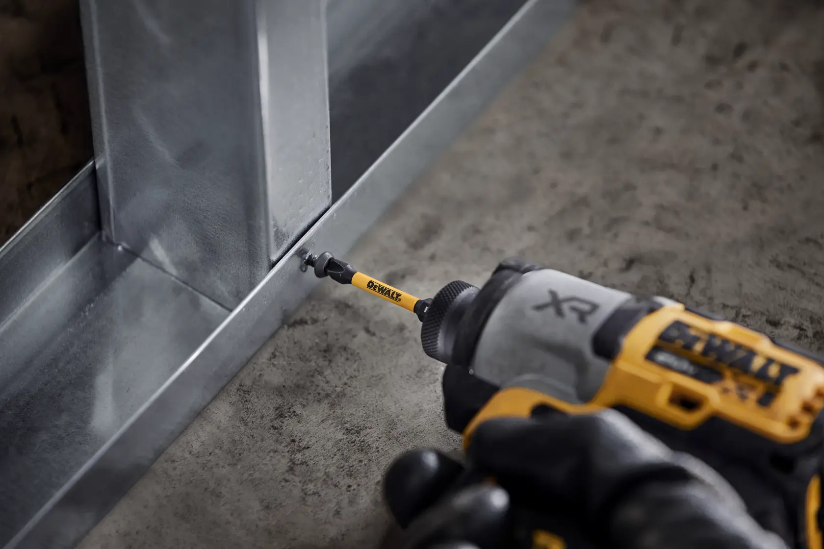 DEWALT drill driving a screw into a metal frame on a construction site floor.