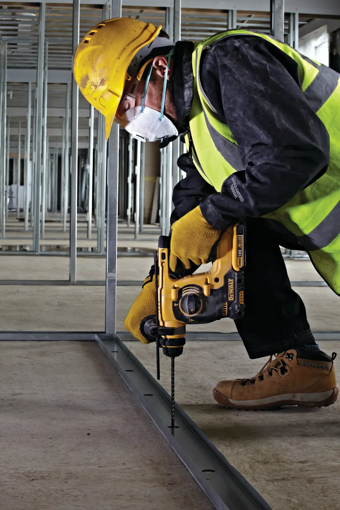 Worker uses DEWALT drill to make holes in metal on a construction site, wearing safety gear and yellow helmet.