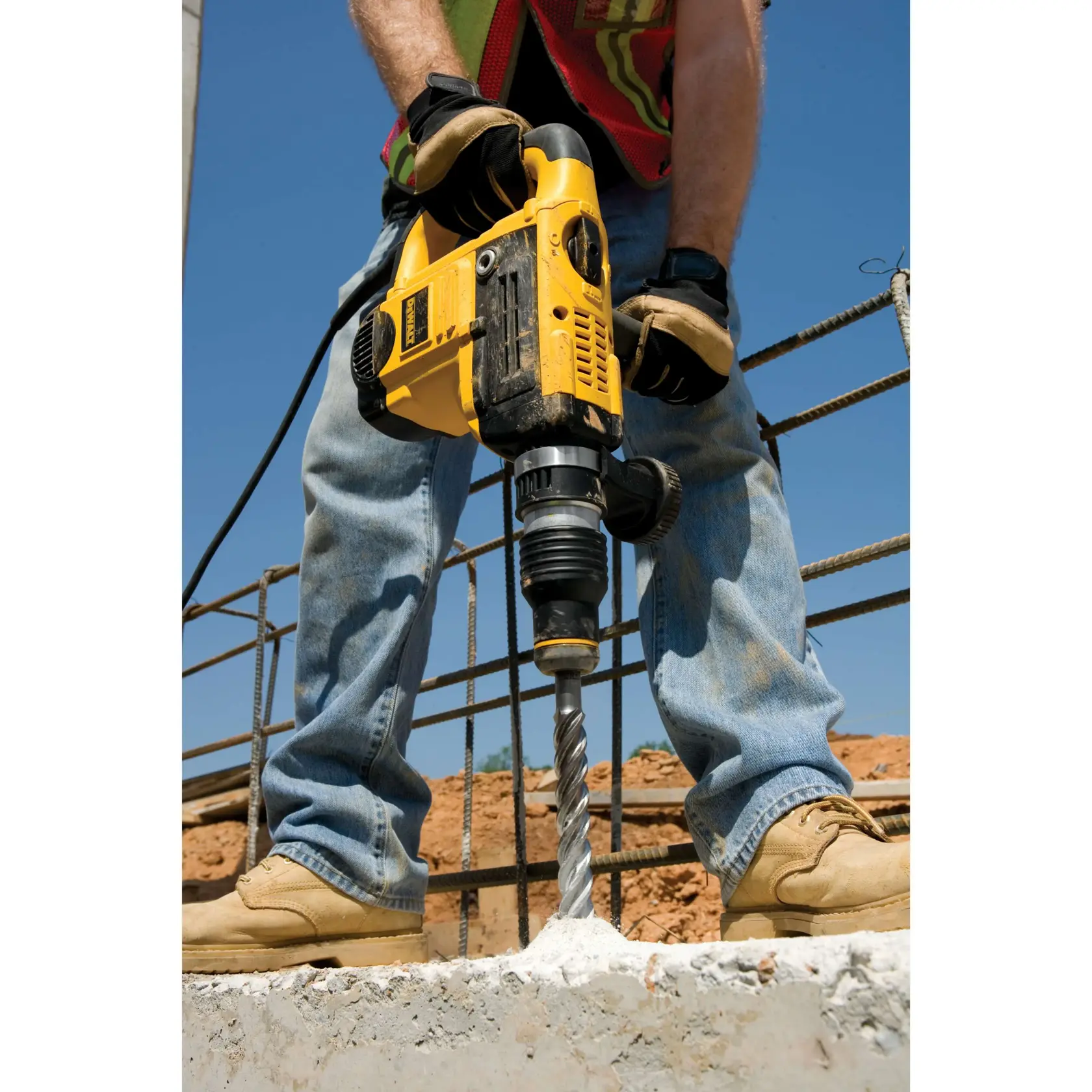 Worker drilling into concrete with a yellow DEWALT rotary hammer drill at a construction site.