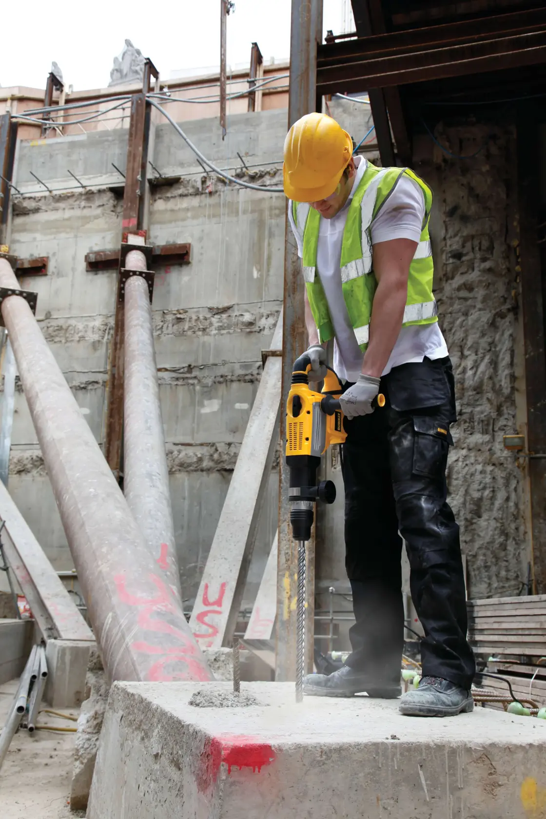 Worker uses DEWALT rotary hammer drill to bore into concrete at a construction site, wearing safety gear.