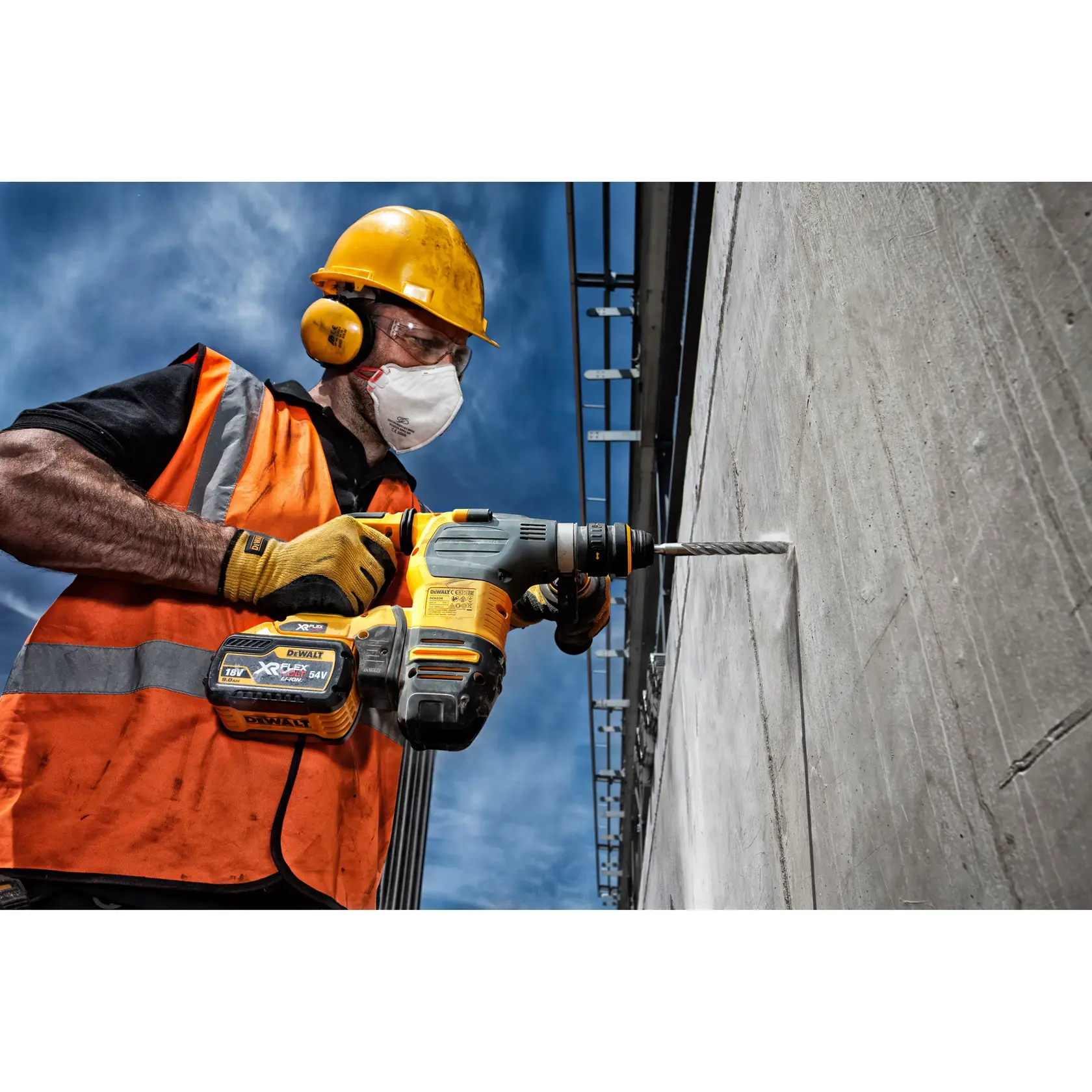 Worker drills concrete wall with a DEWALT rotary hammer using the DT9502 bit. Wears helmet, gloves, safety vest.