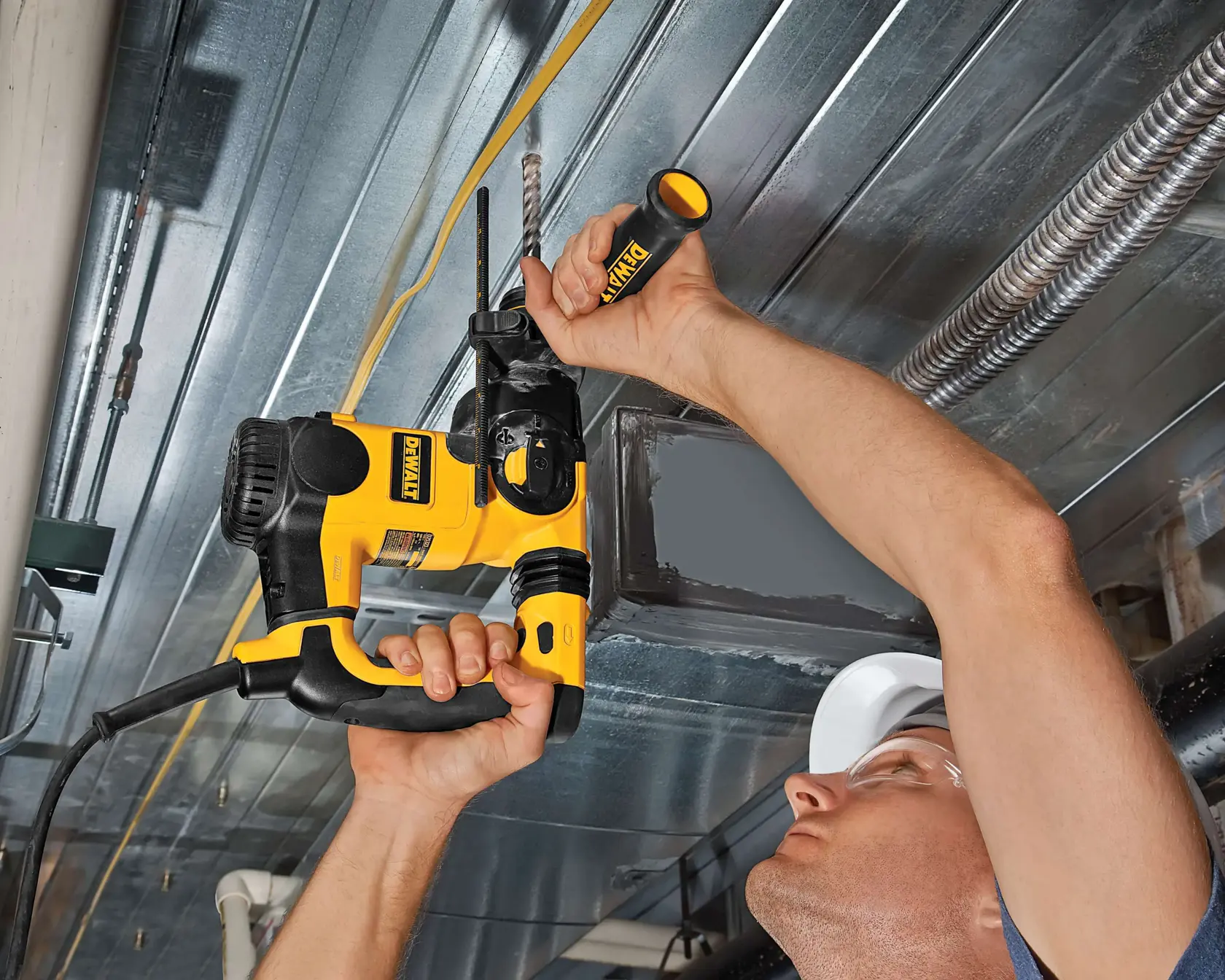 Person drills into metal ceiling using a yellow and black DEWALT power tool with a side handle.