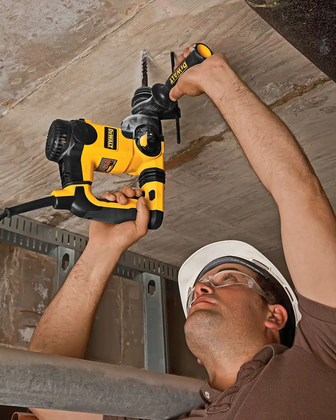 Person using a yellow DEWALT drill to work on a ceiling, wearing a hard hat for safety.