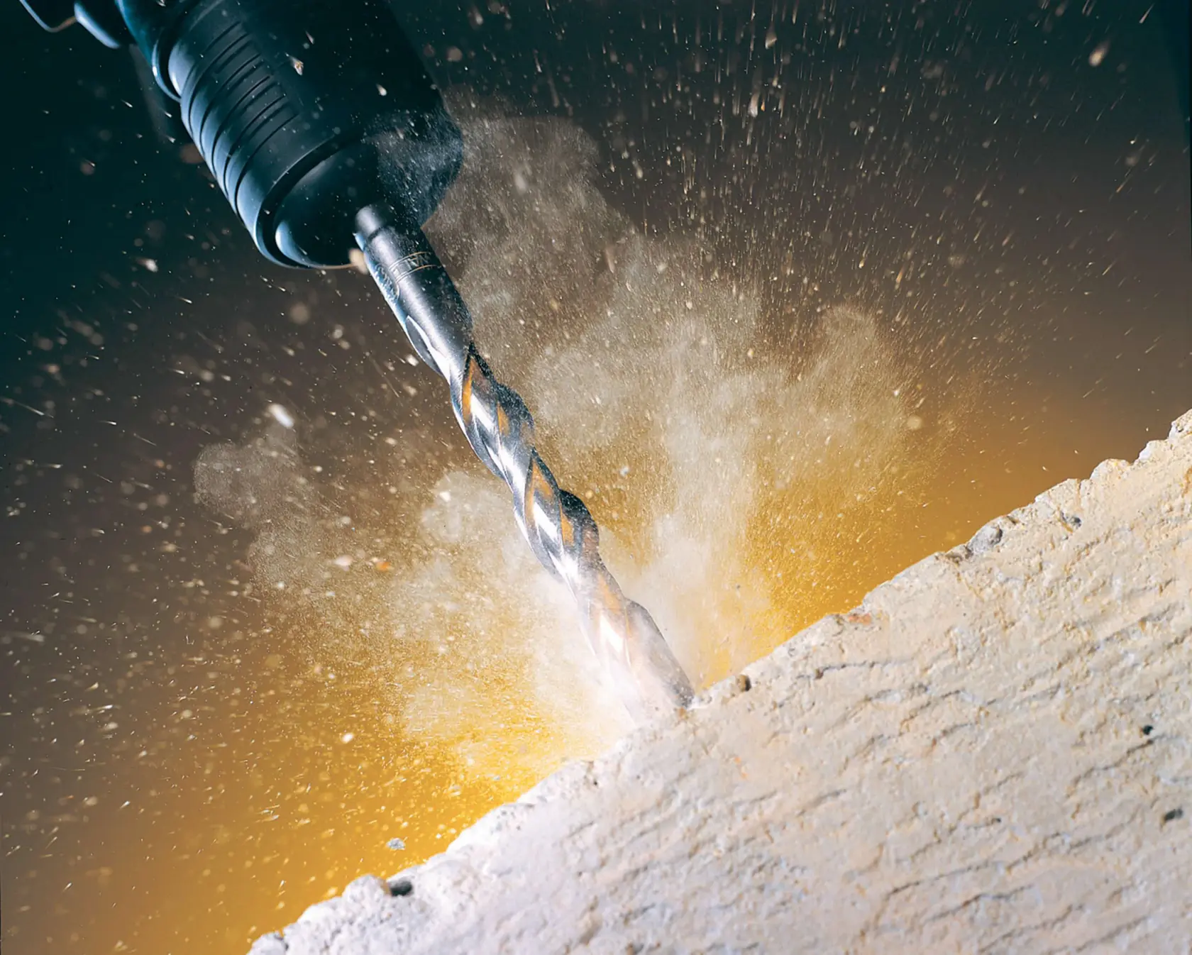 Close-up of a DEWALT drill bit making a hole in concrete, with dust and debris spraying out.
