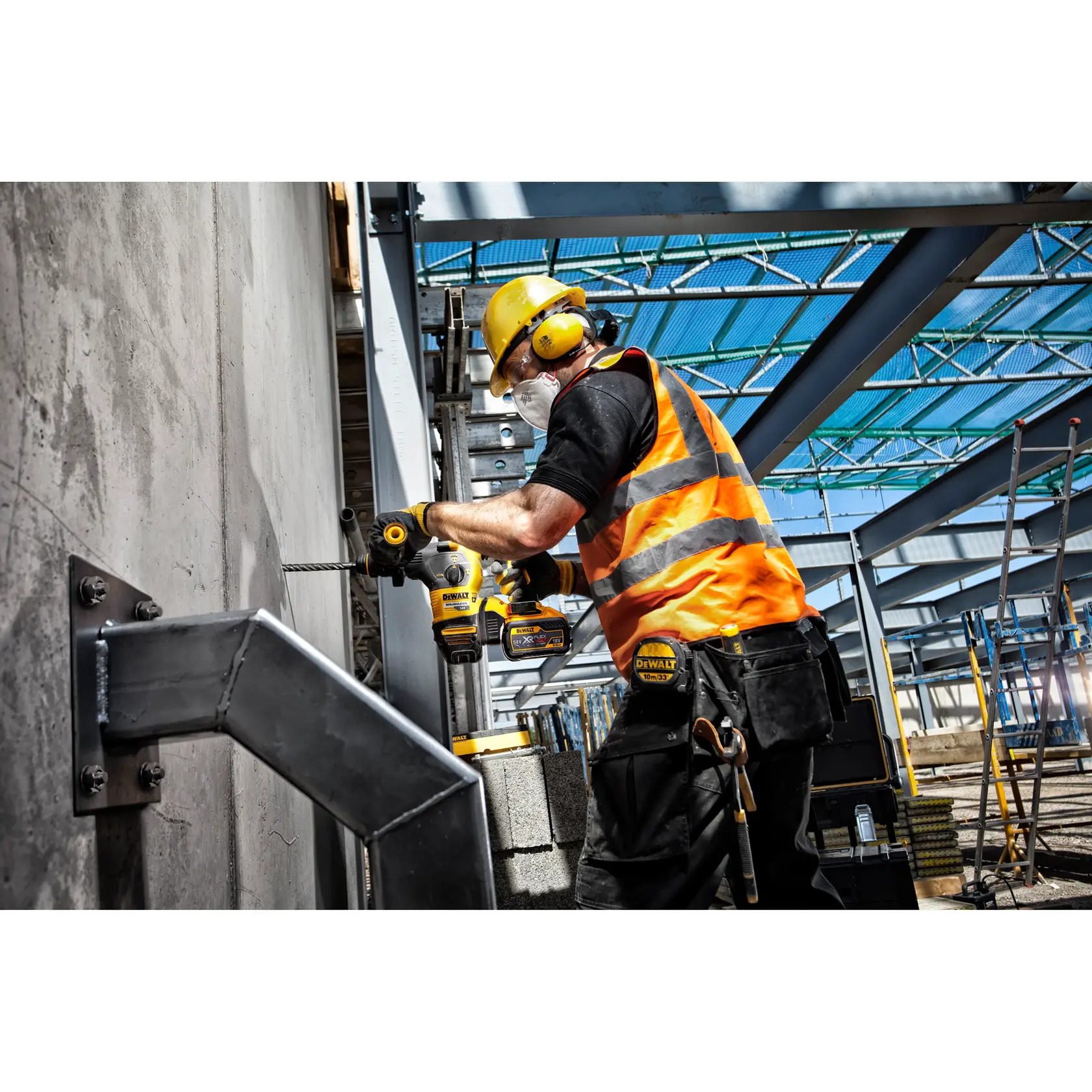 Construction worker uses a DEWALT drill on a concrete wall at an industrial site, wearing safety gear.