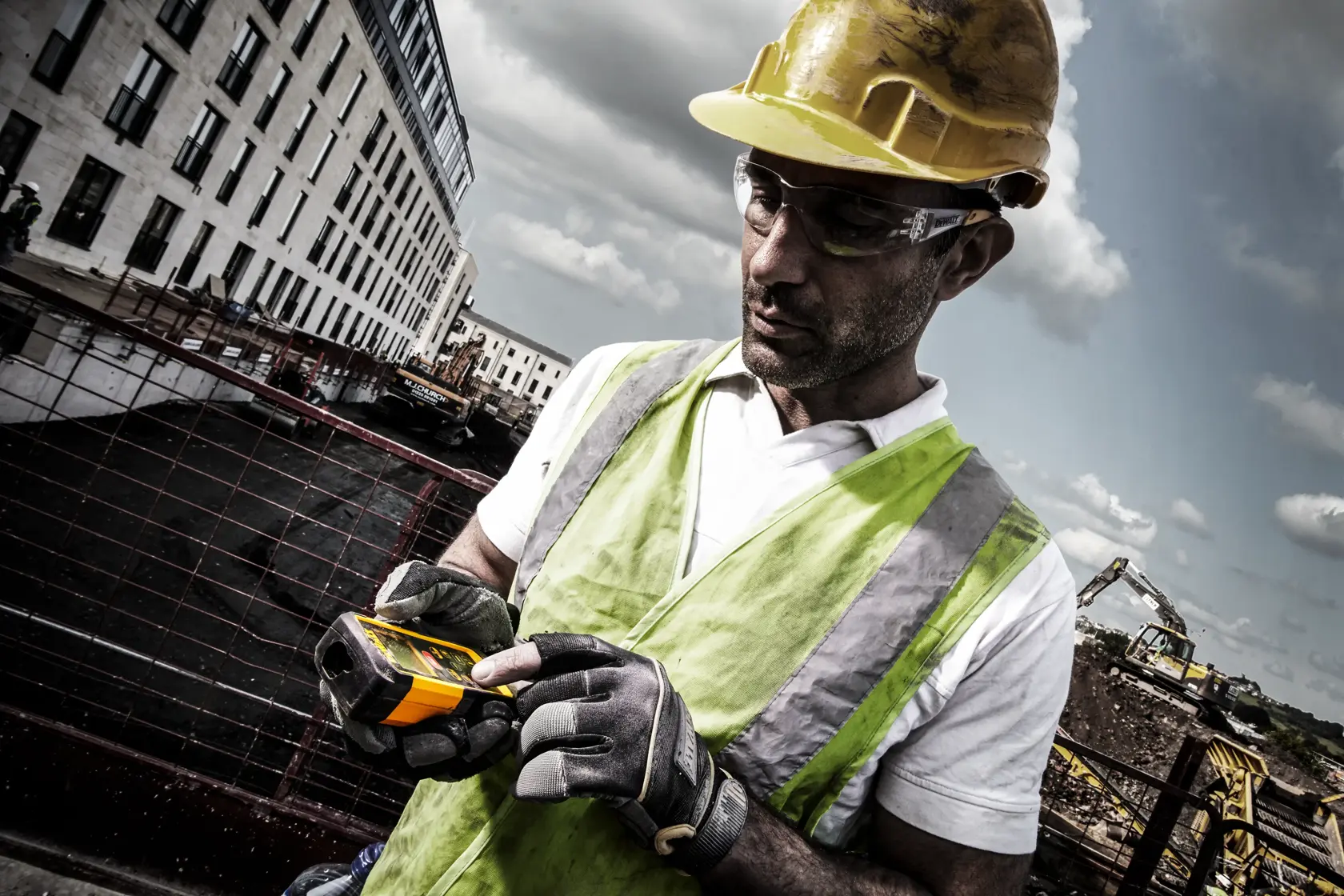 Worker in safety gear uses a DEWALT DW03050 laser distance measurer at a construction site outdoors.