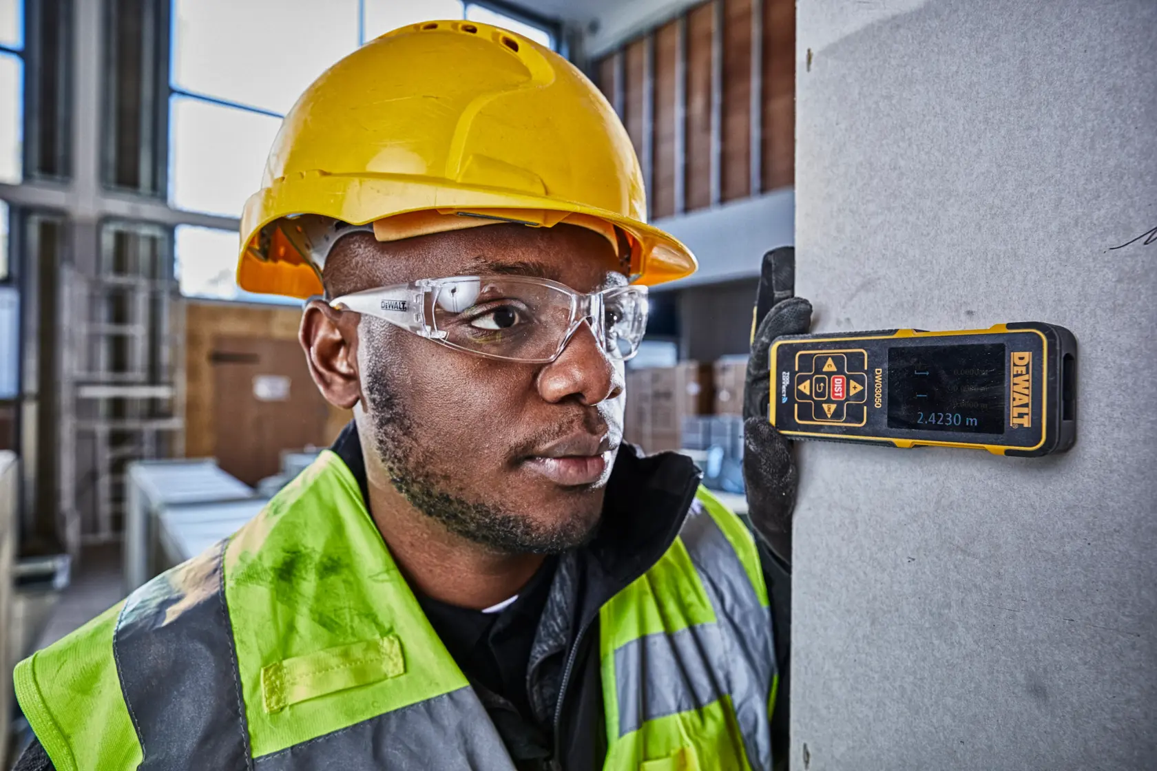 DEWALT DW03050 laser distance measurer used by a worker in safety gear at a construction site.