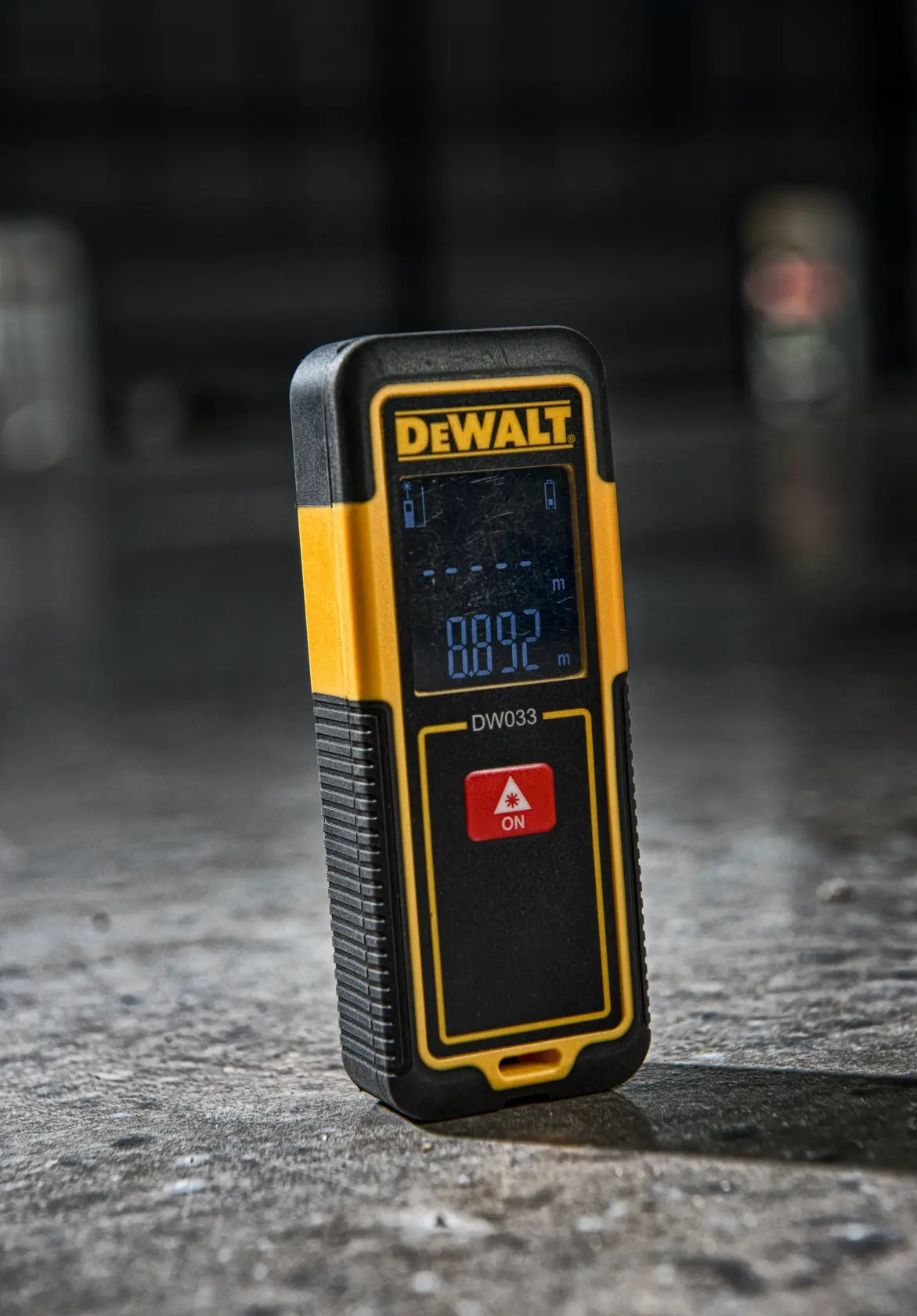 DEWALT DW033 laser distance measurer with a digital screen, yellow and black, standing on a concrete floor.