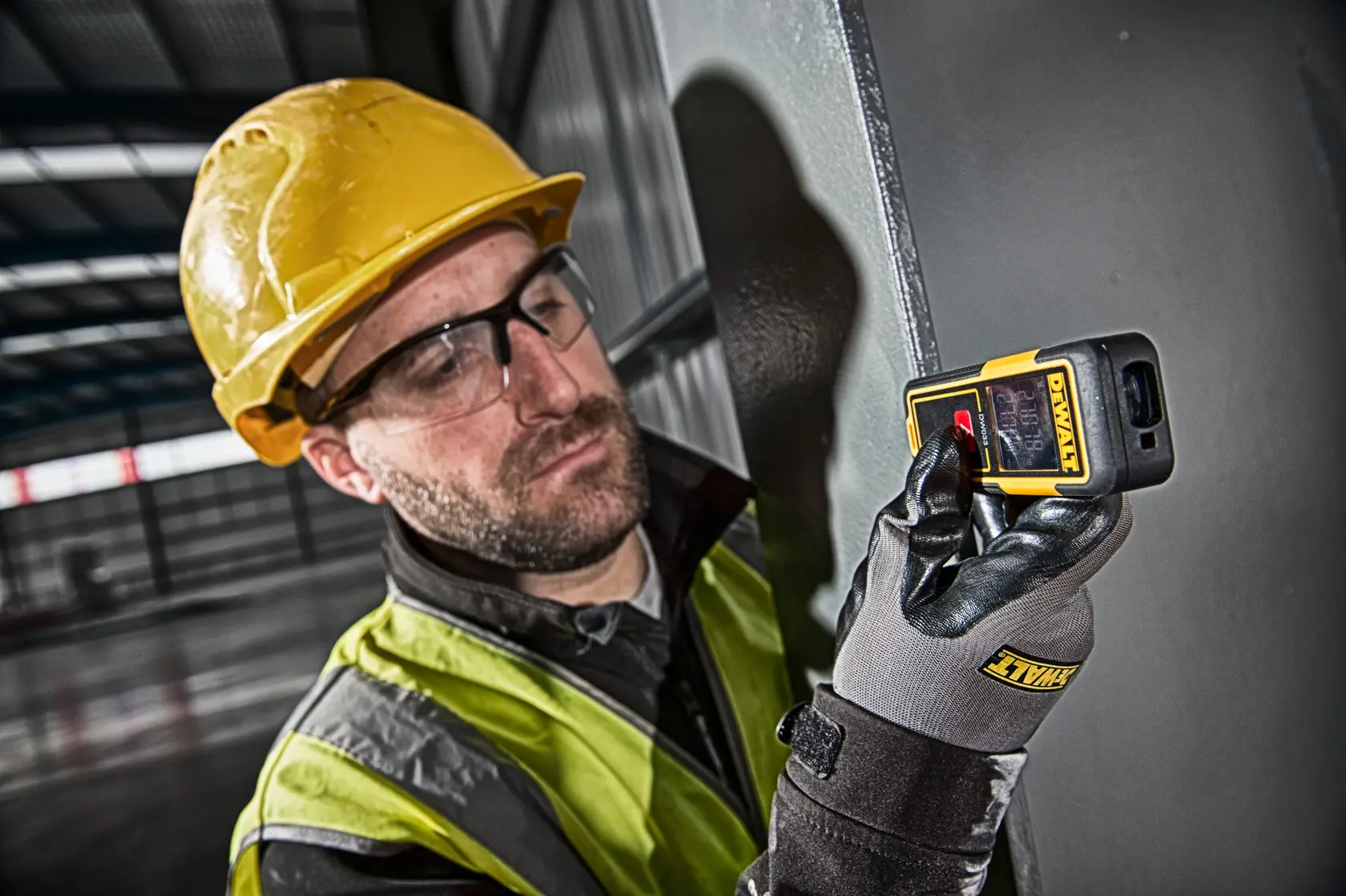 Person in safety gear using a DEWALT DW033 laser distance measurer in an industrial setting.