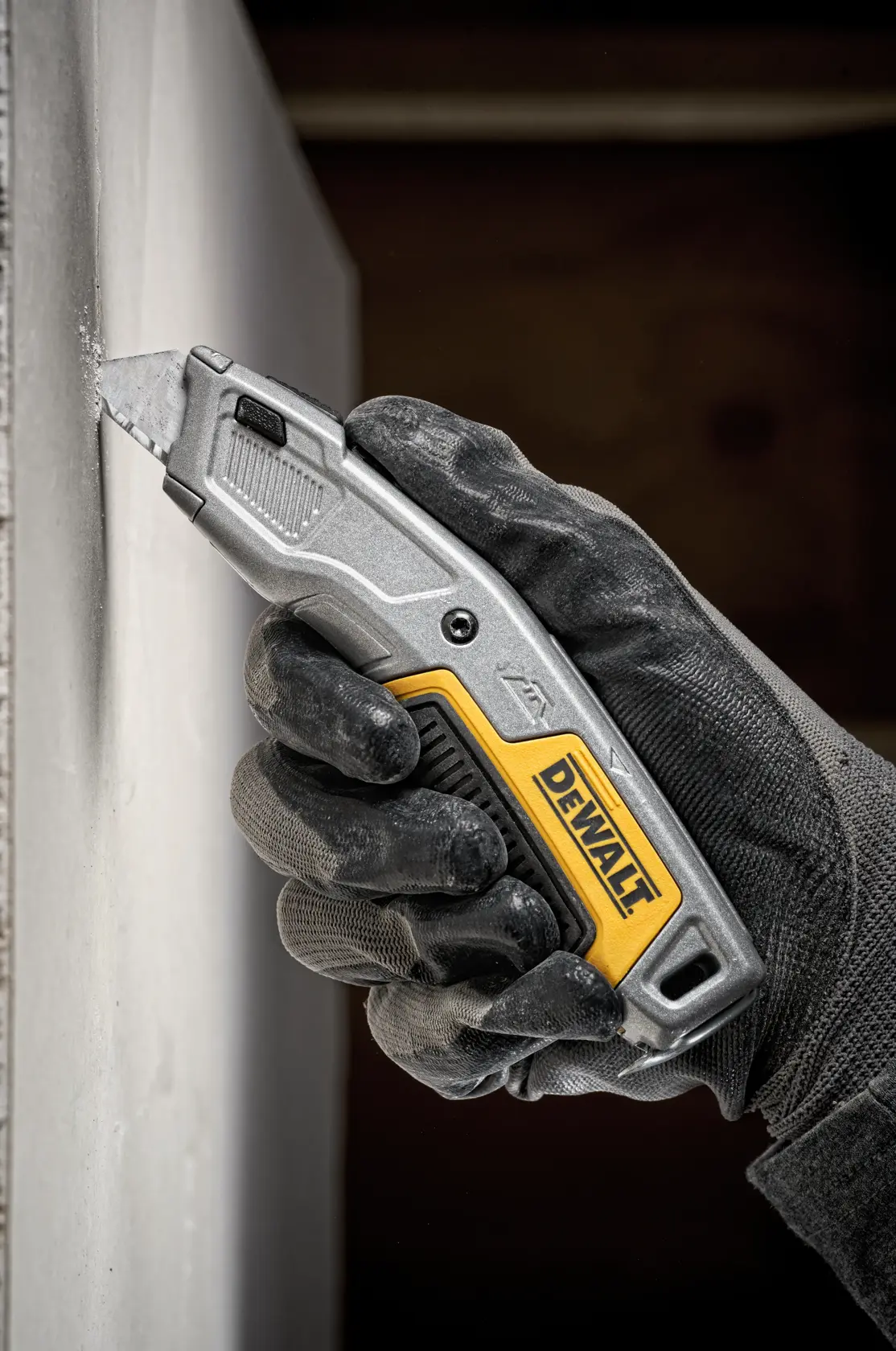 Gloved hand uses a DEWALT utility knife to cut drywall. Close-up of tool and action.