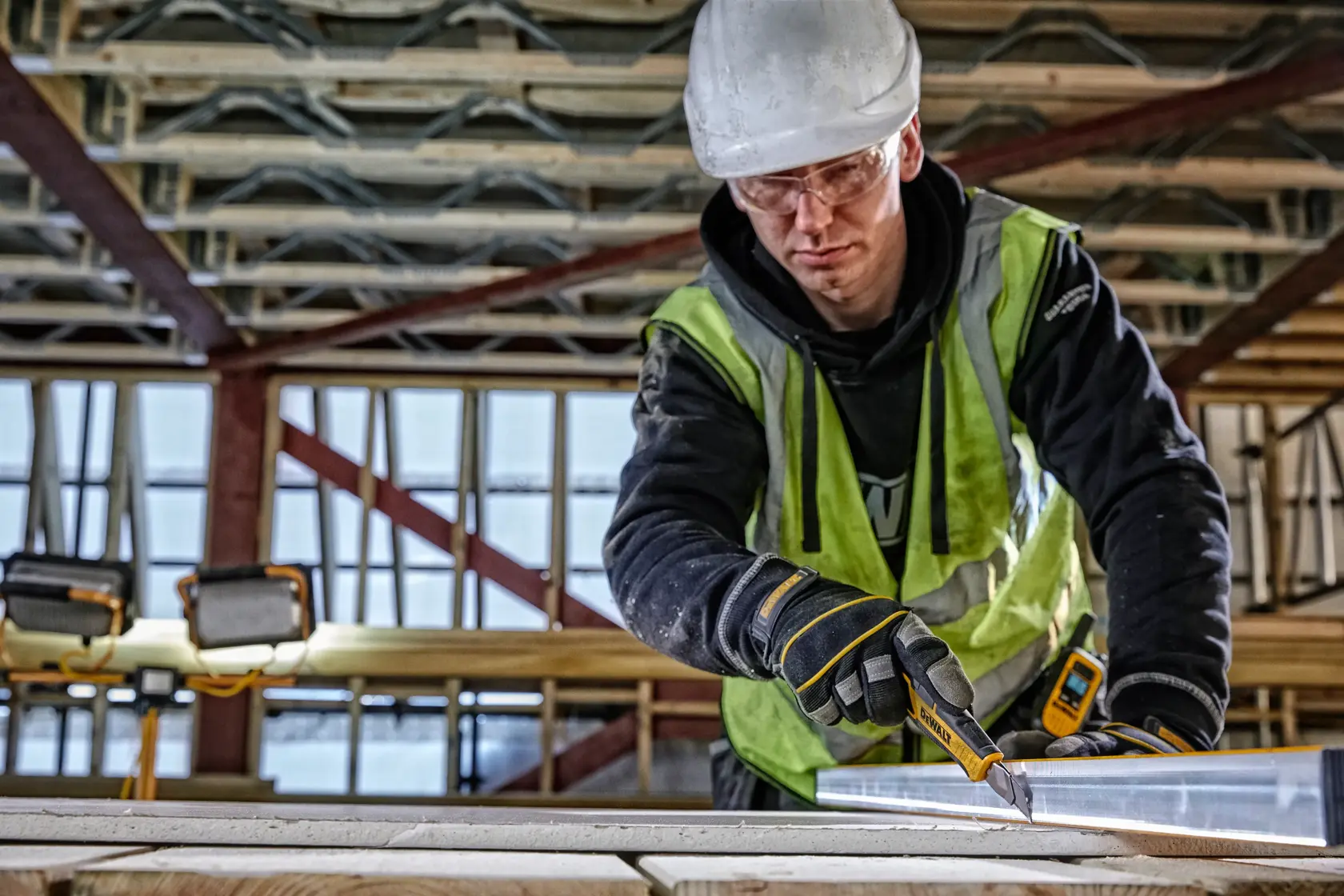 Worker uses DEWALT utility knife to cut material at construction site, wearing safety gear and gloves.