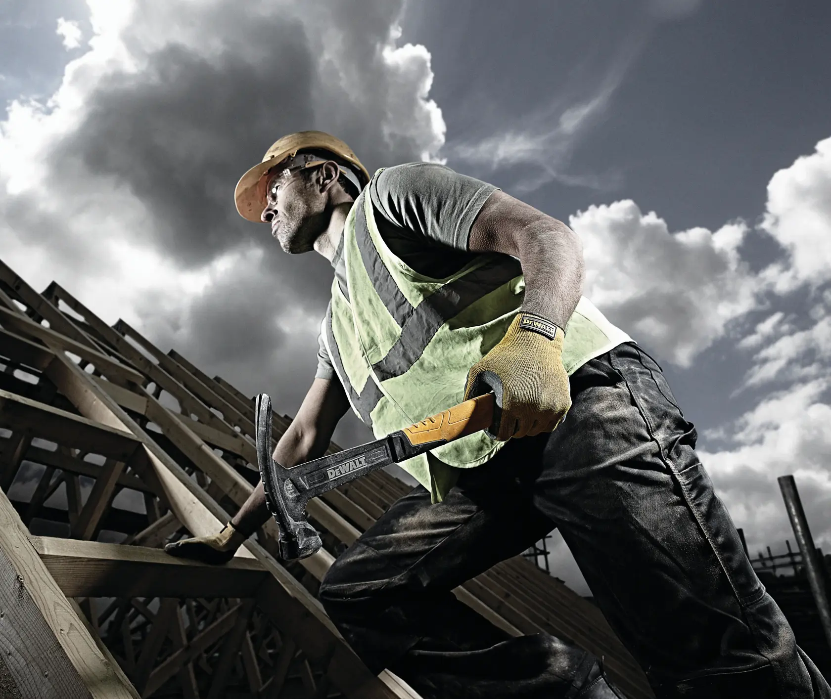 Worker on a roof with DEWALT hammer, safety vest, gloves, and helmet. Wooden beams and cloudy sky in background.