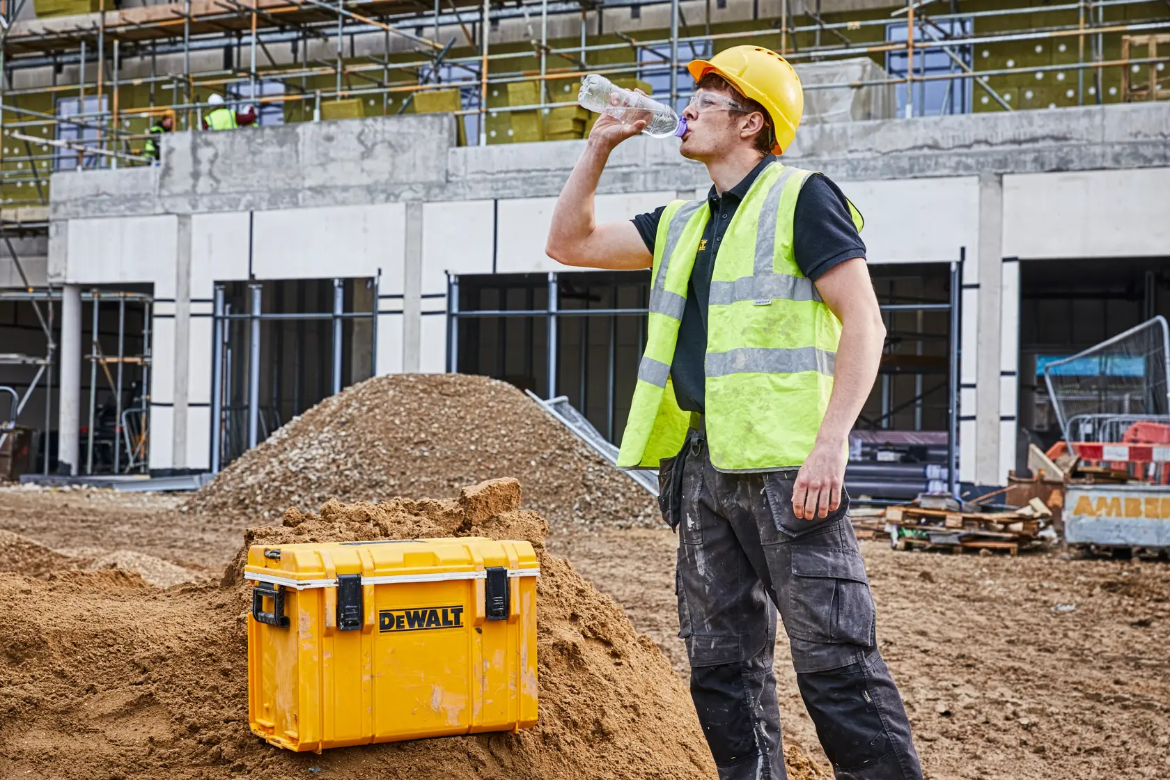 DEWALT storage box on a construction site with a worker in safety gear drinking water nearby.