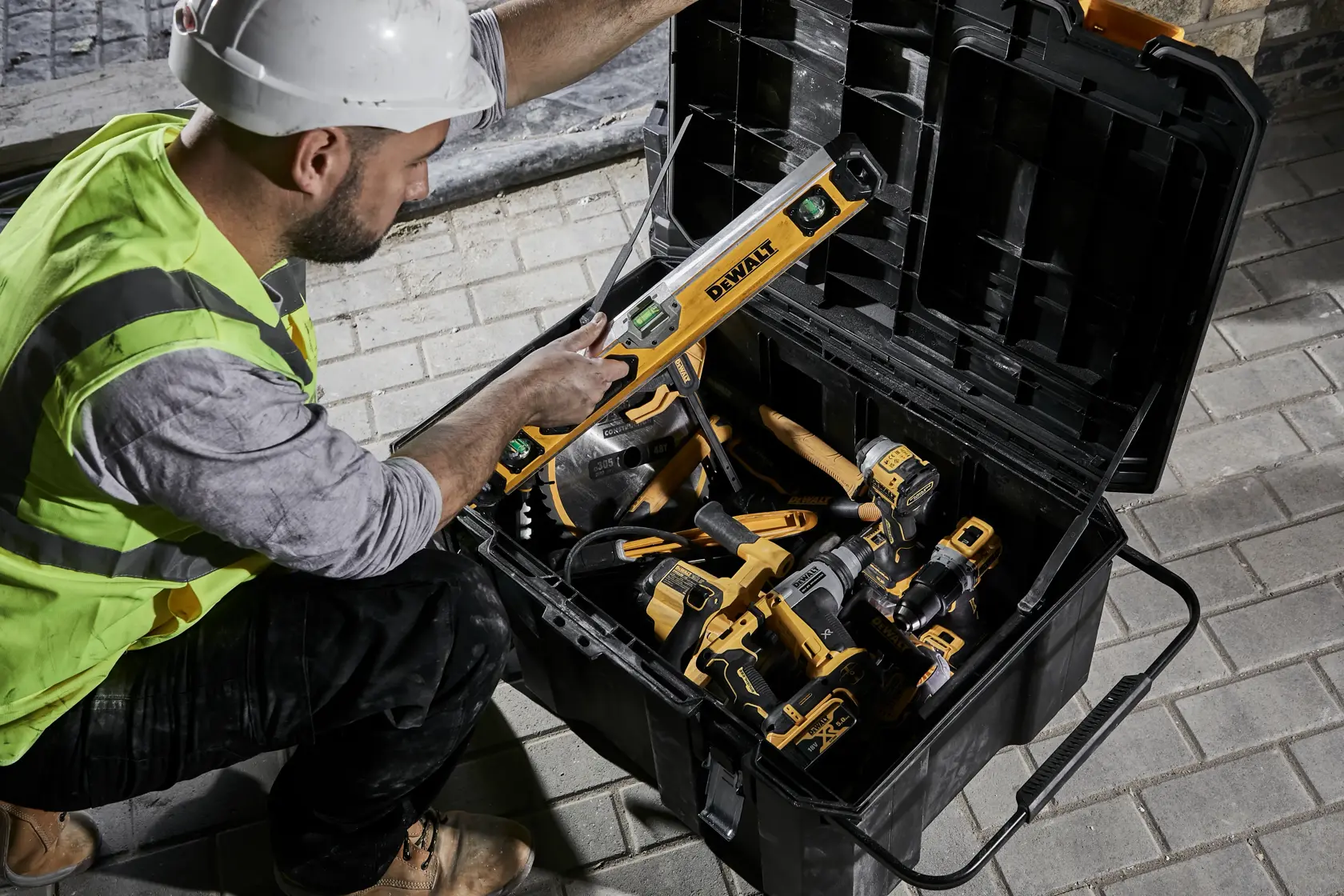 Person with safety gear uses DEWALT tool from a large toolbox full of yellow and black DEWALT power tools.