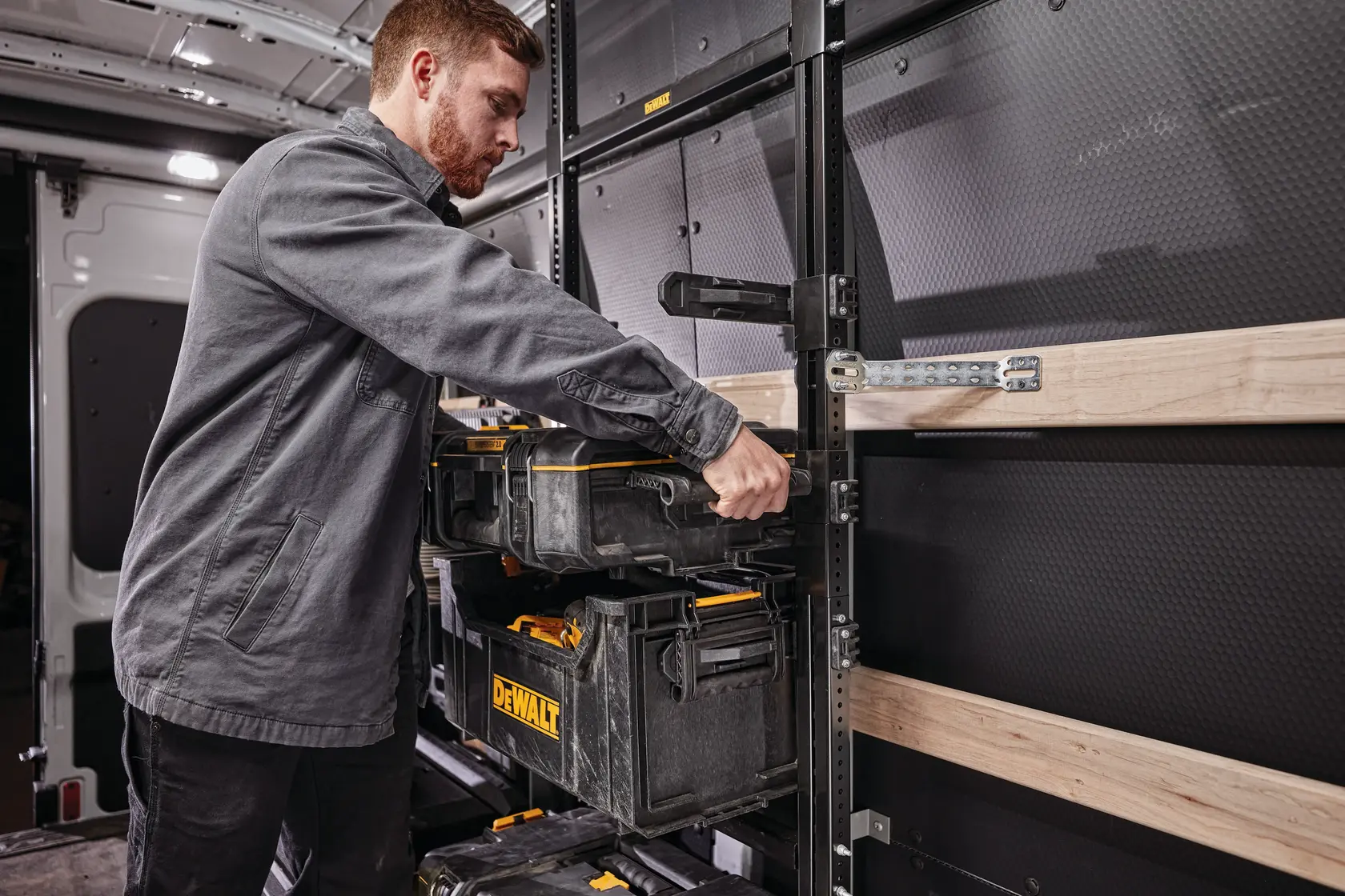 Person organizing DEWALT toolboxes on a shelving system inside a work van.