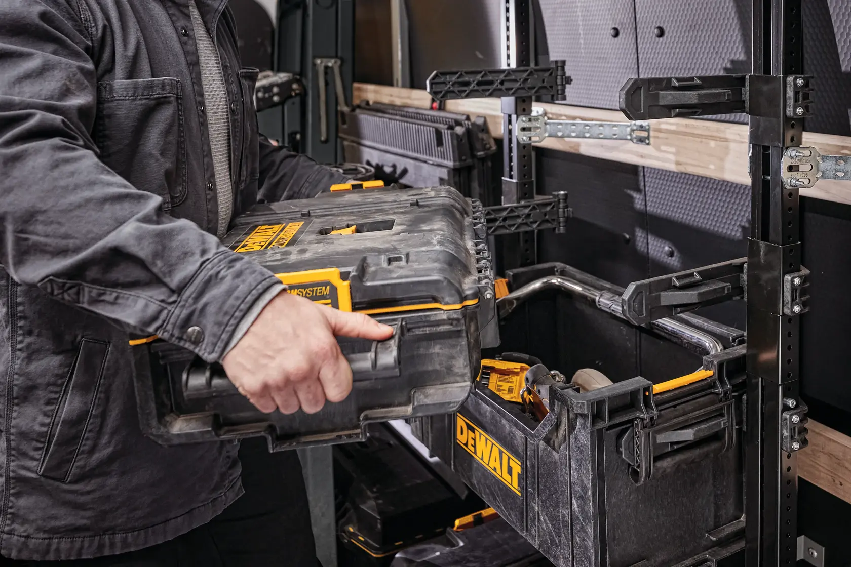 Person places a DEWALT toolbox onto modular rack system inside a workshop or utility vehicle.