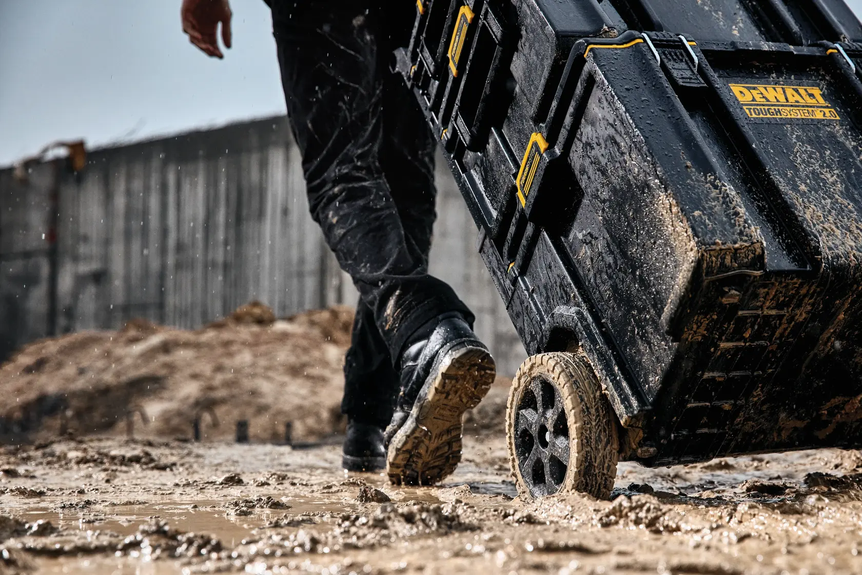 Muddy DEWALT ToughSystem 2.0 toolbox on wheels being pulled across a wet, muddy construction site.