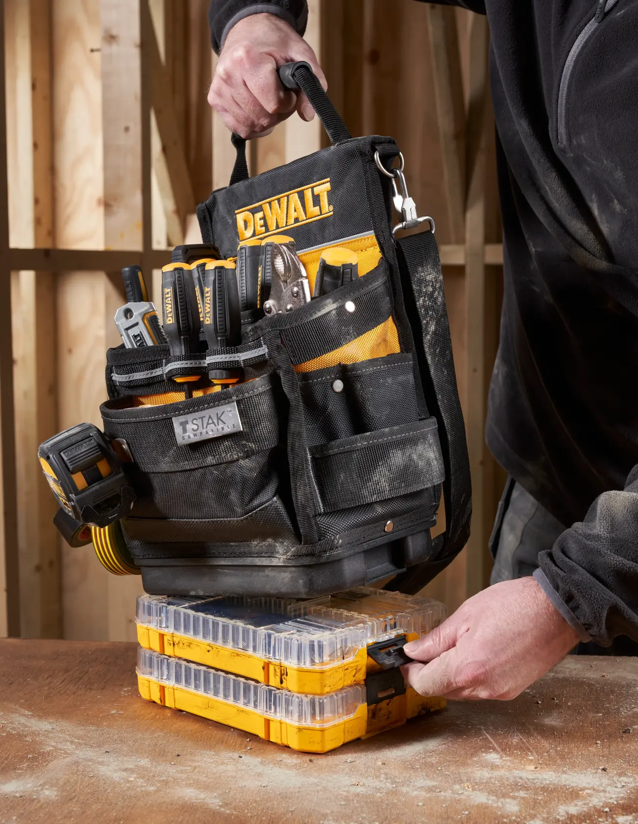 DEWALT tool bag with tools set on yellow stackable organizers on a workbench, handled by a person in workwear.