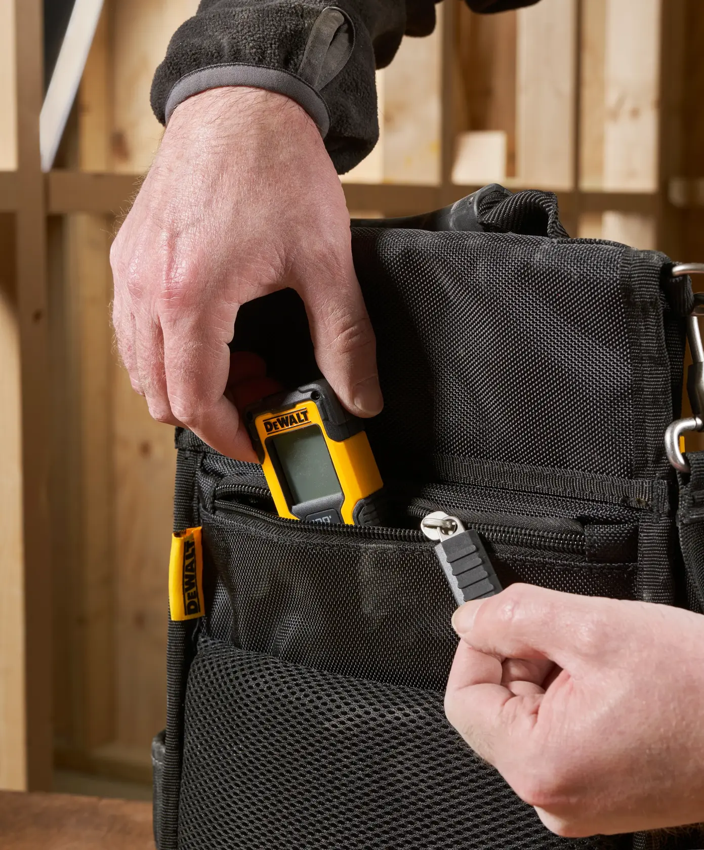 Hand places DEWALT device and tool bit into black zippered bag pocket in a workshop setting.