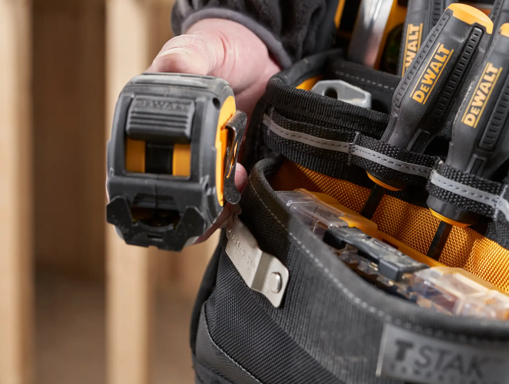 Close-up of a DEWALT tool belt with hand holding tape measure and screwdrivers in pockets.