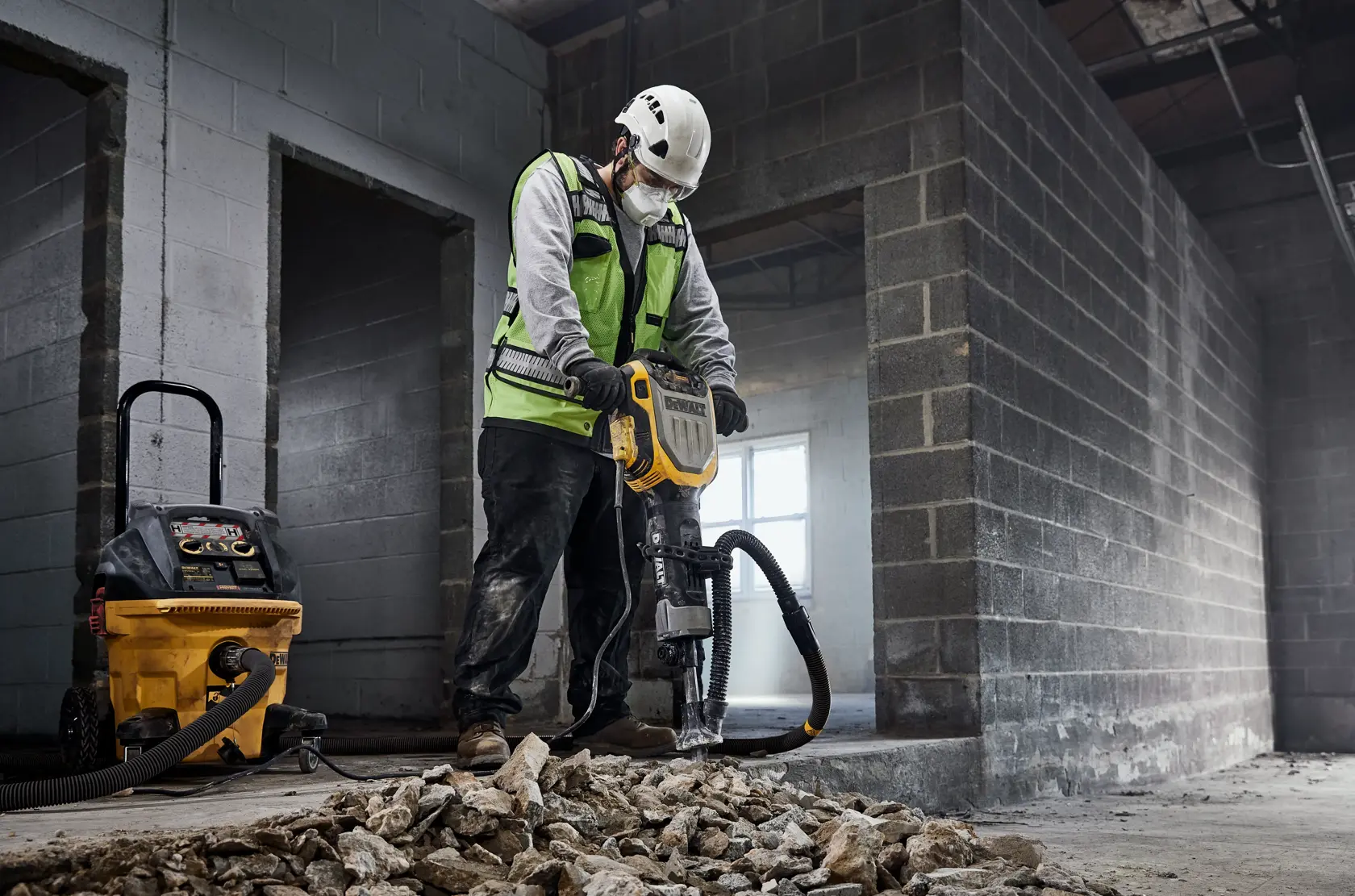 Worker uses DEWALT demolition tool with vacuum in construction site, breaking concrete rubble.